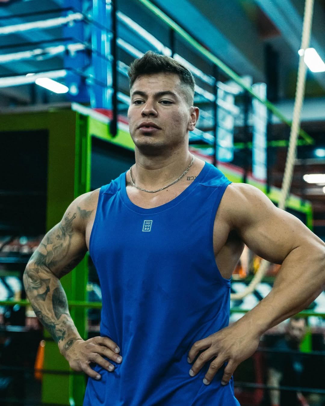Cristian Castaño standing confidently in a gym, wearing a blue tank top and looking focused after training.